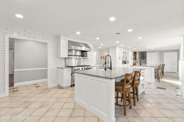79 Cypress Neck Rd, Lincroft, NJ 07738 - kitchen with wall chimney exhaust hood, high end stove, a large island with sink, light tile patterned floors, and a breakfast bar