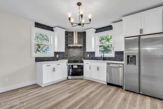 420 Philadelphia Ave, Egg Harbor City, NJ 08215 - kitchen featuring wall chimney range hood, appliances with stainless steel finishes, a chandelier, backsplash, and white cabinetry