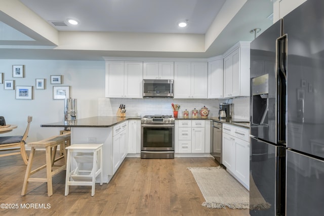 26 9th Ave Unit 105, Ortley Beach, NJ 08751 - kitchen featuring stainless steel appliances, a peninsula, dark countertops, tasteful backsplash, and white cabinetry