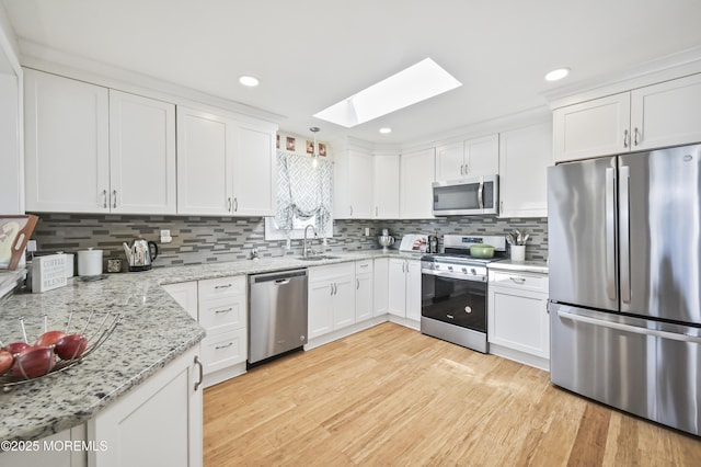 25 Tropicana Ct, Toms River, NJ 08757 - kitchen with stainless steel appliances, a skylight, light wood-style flooring, white cabinetry, and backsplash