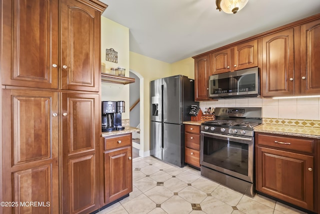 41 Alan Ter, Howell, NJ 07731 - kitchen featuring appliances with stainless steel finishes, decorative backsplash, arched walkways, light stone counters, and brown cabinetry