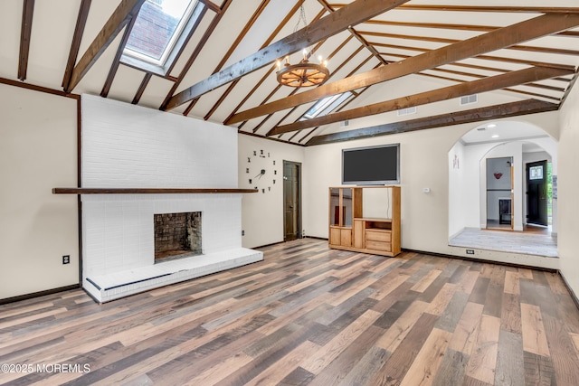 215 Sunset Ln, Howell, NJ 07731 - unfurnished living room featuring a skylight, high vaulted ceiling, a fireplace, arched walkways, and wood finished floors