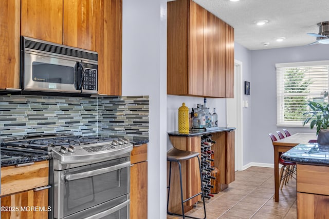 707 Cambridge Rd, Lanoka Harbor, NJ 08734 - kitchen featuring appliances with stainless steel finishes, decorative backsplash, dark stone counters, light tile patterned flooring, and brown cabinetry