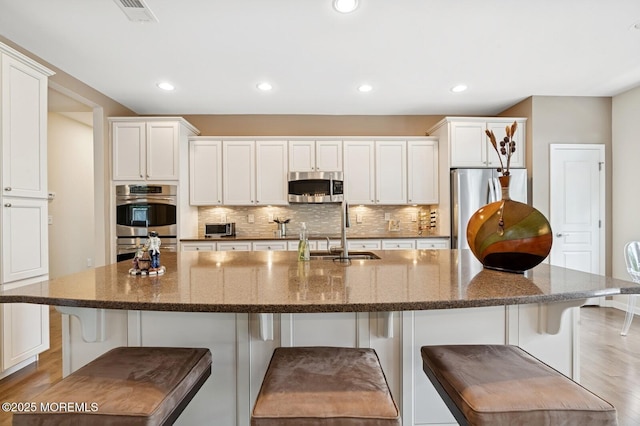 6 Day Star Rd, Manalapan, NJ 07726 - kitchen featuring stainless steel appliances, light wood-type flooring, decorative backsplash, white cabinets, and a breakfast bar