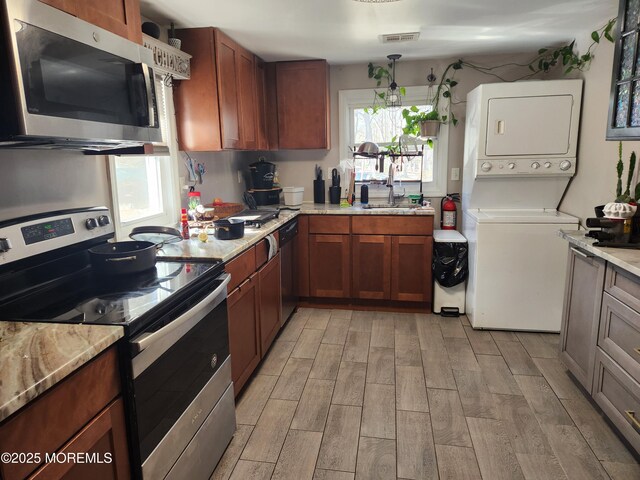 517 Newtons Corner Rd, Howell, NJ 07731 - kitchen with appliances with stainless steel finishes, stacked washing machine and dryer, light wood-style floors, brown cabinets, and light stone countertops