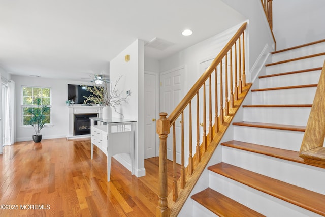 9 Nutmeg Ct, Tinton Falls, NJ 07753 - staircase featuring wood finished floors, a glass covered fireplace, a ceiling fan, and recessed lighting