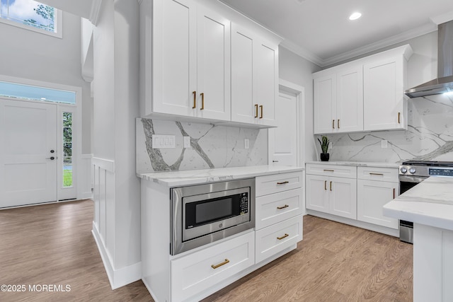 127 Rogers St, Bayville, NJ 08721 - kitchen featuring stainless steel appliances, wall chimney range hood, healthy amount of natural light, ornamental molding, and white cabinetry