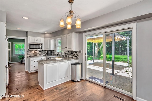 25 Forman Ln, Manalapan, NJ 07726 - kitchen with stainless steel microwave, a peninsula, white cabinets, a chandelier, and backsplash