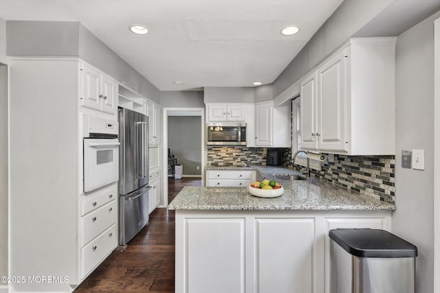 25 Forman Ln, Manalapan, NJ 07726 - kitchen with stainless steel appliances, a peninsula, dark wood-style floors, decorative backsplash, and light stone countertops