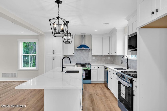 629 Monmouth Ave, Toms River, NJ 08757 - kitchen featuring wall chimney range hood, stainless steel appliances, a chandelier, an island with sink, and light wood-style floors