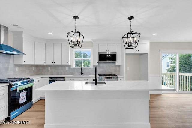 629 Monmouth Ave, Toms River, NJ 08757 - kitchen featuring stainless steel appliances, wall chimney range hood, a chandelier, light wood-style flooring, and white cabinetry