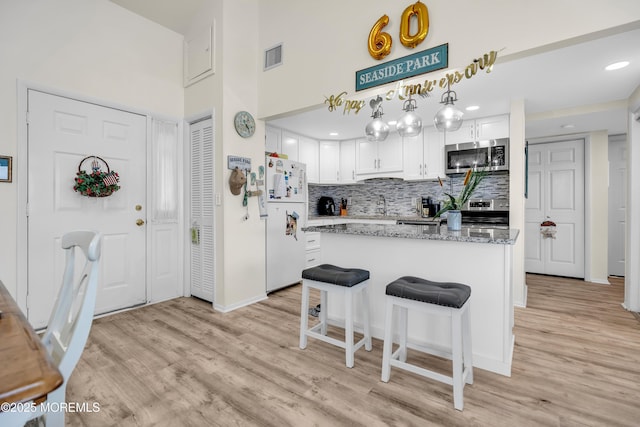 2108 SE Central Ave Unit 10, South Seaside Park, NJ 08752 - kitchen featuring white cabinets, appliances with stainless steel finishes, light wood-type flooring, tasteful backsplash, and light stone counters