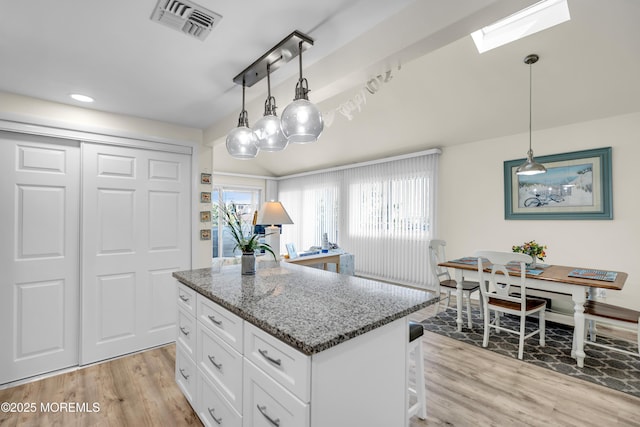 2108 SE Central Ave Unit 10, South Seaside Park, NJ 08752 - kitchen with stone countertops, white cabinets, light wood-type flooring, a kitchen island, and decorative light fixtures