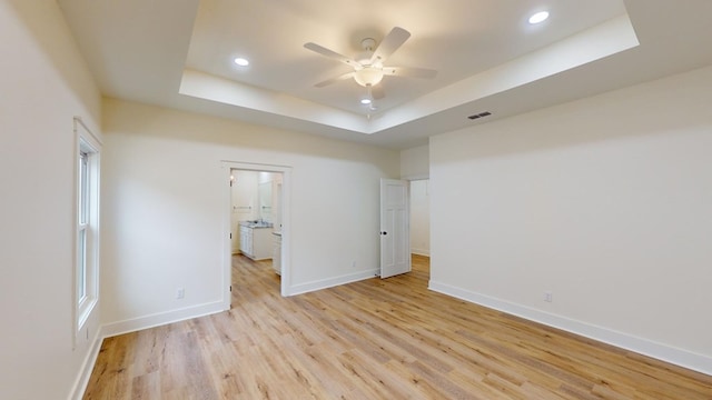 spare room with ceiling fan, light wood-type flooring, and a tray ceiling