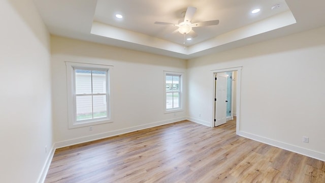 unfurnished room featuring a raised ceiling, ceiling fan, and light hardwood / wood-style floors