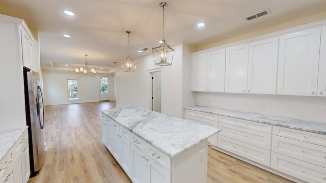 kitchen featuring white cabinetry, light stone counters, hanging light fixtures, and a kitchen island