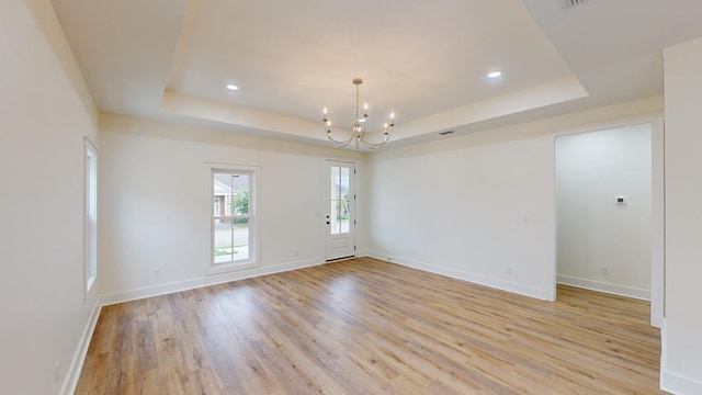 spare room with a raised ceiling, light wood-type flooring, and a chandelier