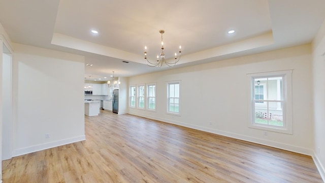 unfurnished living room with light hardwood / wood-style floors, a chandelier, and a tray ceiling