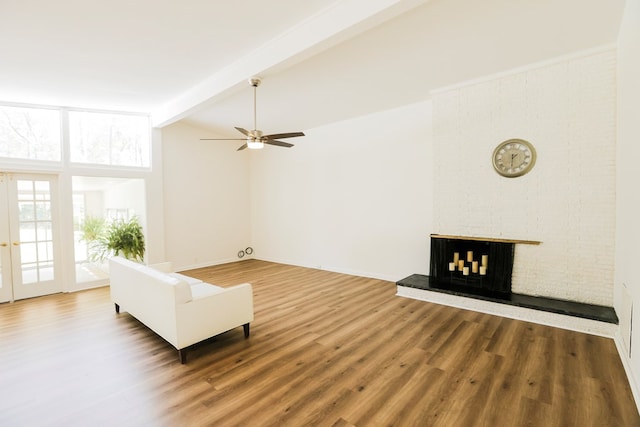 living area with baseboards, a fireplace, wood finished floors, ceiling fan, and vaulted ceiling with beams