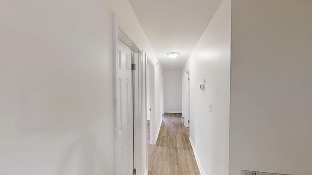 corridor featuring light wood-type flooring and baseboards