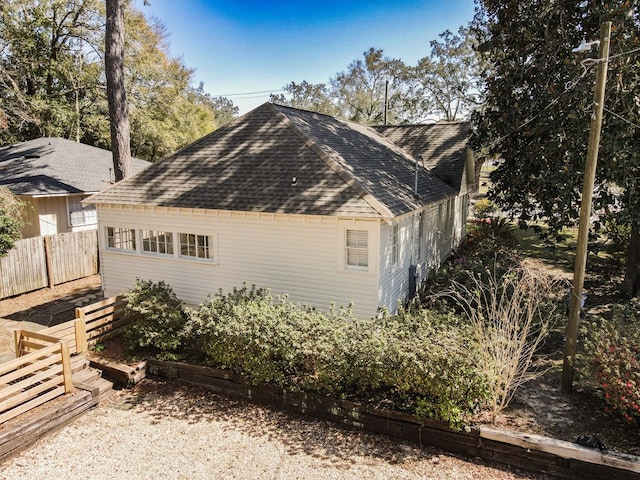 view of home's exterior with roof with shingles and fence