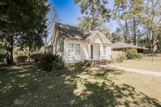 view of front of home featuring roof with shingles, a chimney, a front yard, and fence