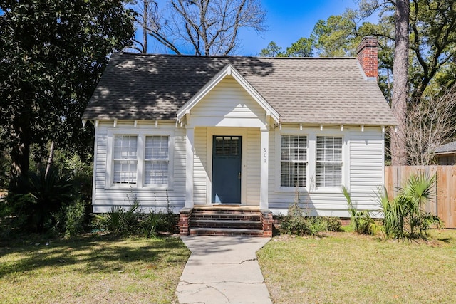 view of front facade featuring a shingled roof, a front lawn, fence, and a chimney