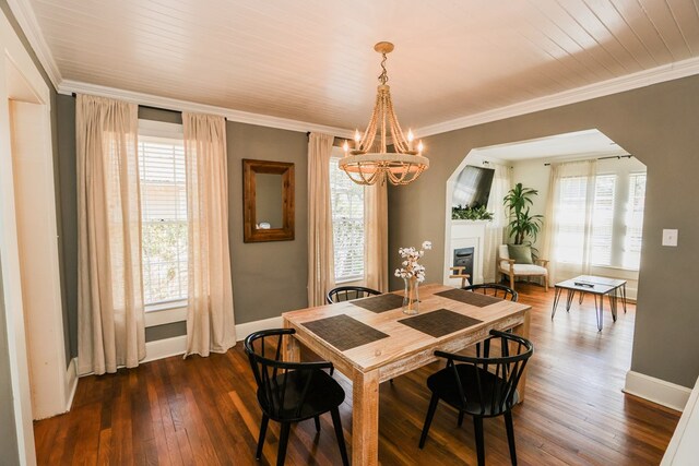 dining room with ornamental molding, dark wood-style floors, arched walkways, a fireplace, and a chandelier