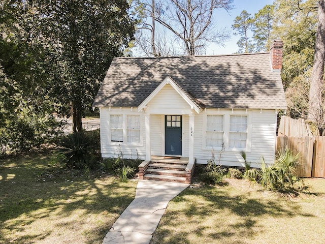 view of front facade with a chimney, roof with shingles, a front yard, and fence