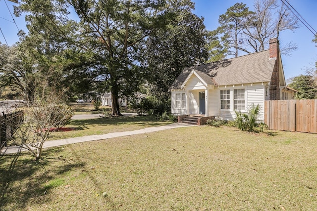 view of front facade with a chimney, a shingled roof, a front yard, and fence