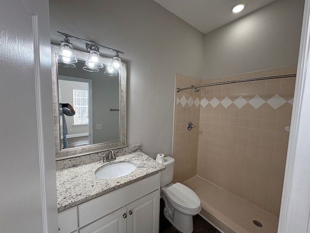 bathroom with tiled shower, toilet, vanity, and a textured wall