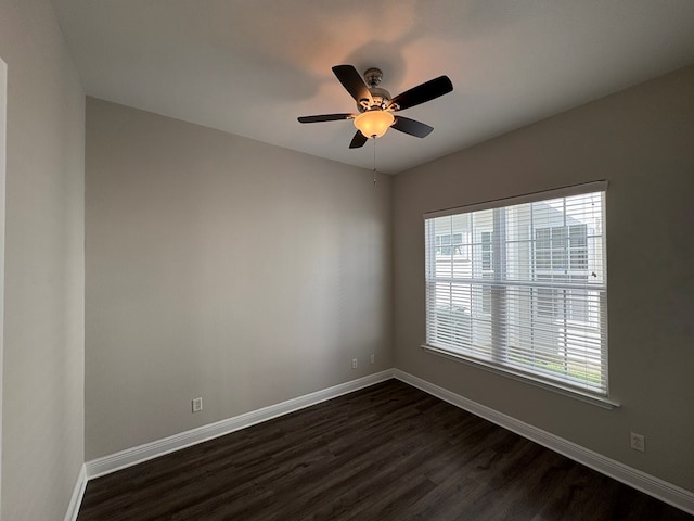 empty room featuring a wealth of natural light, baseboards, dark wood-style floors, and a ceiling fan