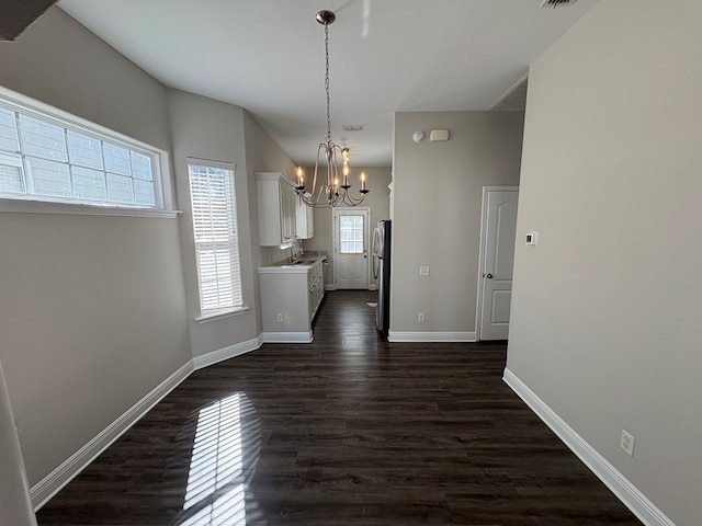 unfurnished dining area with visible vents, baseboards, dark wood-style flooring, a sink, and a notable chandelier