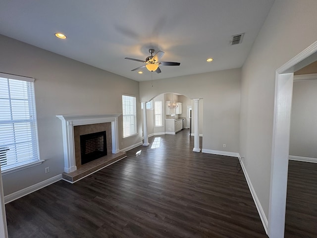 unfurnished living room with visible vents, baseboards, a fireplace, arched walkways, and dark wood-style flooring