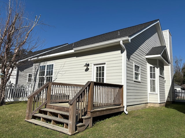 back of house with a deck, a lawn, fence, and roof with shingles