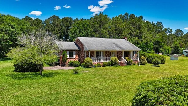 single story home featuring covered porch, a front lawn, and a wooded view