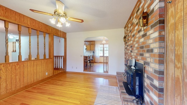 living room with light wood-style flooring, arched walkways, ceiling fan, wooden walls, and baseboards