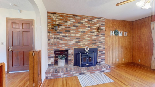 unfurnished living room featuring wood finished floors, arched walkways, a wood stove, baseboards, and wood walls