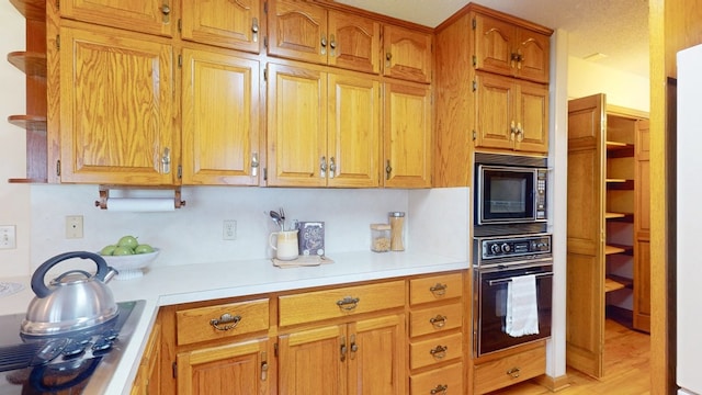 kitchen with black appliances, light countertops, brown cabinetry, and open shelves