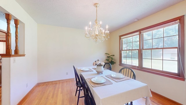 dining space featuring light wood-type flooring, a chandelier, baseboards, and a textured ceiling