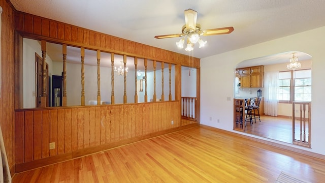 unfurnished room featuring light wood-style flooring, a chandelier, arched walkways, wooden walls, and a ceiling fan