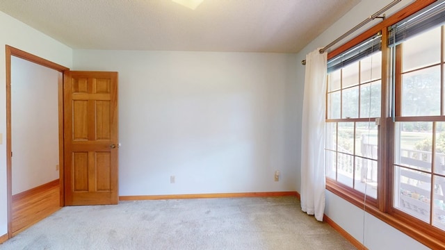 empty room featuring healthy amount of natural light, light carpet, and baseboards