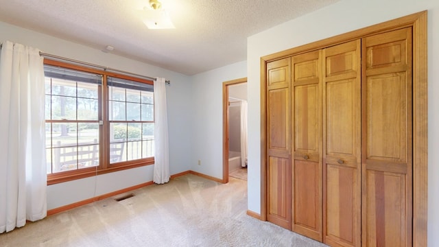 unfurnished bedroom featuring light carpet, baseboards, a closet, and a textured ceiling