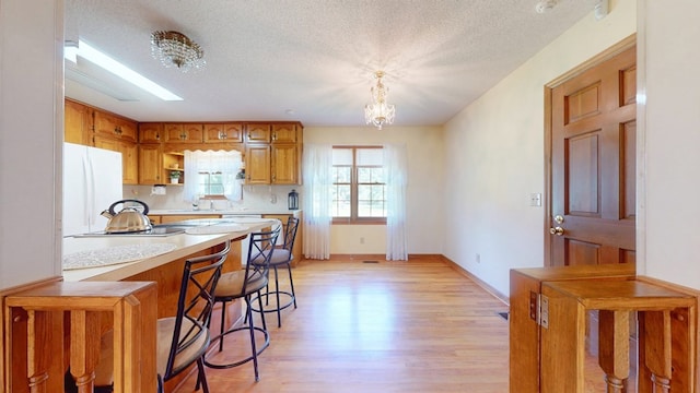 kitchen featuring freestanding refrigerator, light countertops, brown cabinets, light wood-style floors, and a chandelier