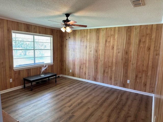 spare room featuring wood walls, dark hardwood / wood-style flooring, ornamental molding, ceiling fan, and a textured ceiling