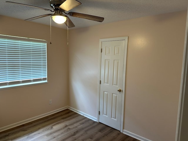 empty room with ceiling fan, wood-type flooring, and a textured ceiling