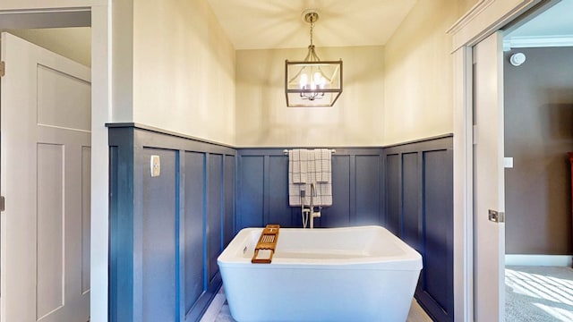 bathroom with a chandelier, a decorative wall, wainscoting, and a freestanding tub