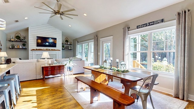 dining area with visible vents, a fireplace, light wood finished floors, lofted ceiling, and ceiling fan