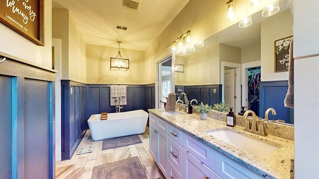 full bath with visible vents, a sink, wainscoting, double vanity, and a soaking tub