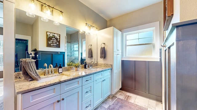 full bathroom with a shower with door, double vanity, and a sink